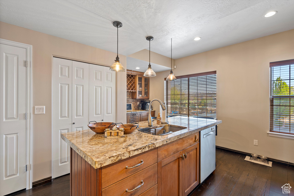 Kitchen featuring a kitchen island with sink, sink, backsplash, dark hardwood / wood-style flooring, and pendant lighting