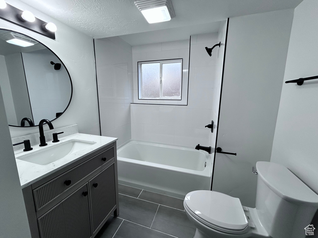 Full bathroom with large vanity, tile floors, toilet, and tiled shower / bath