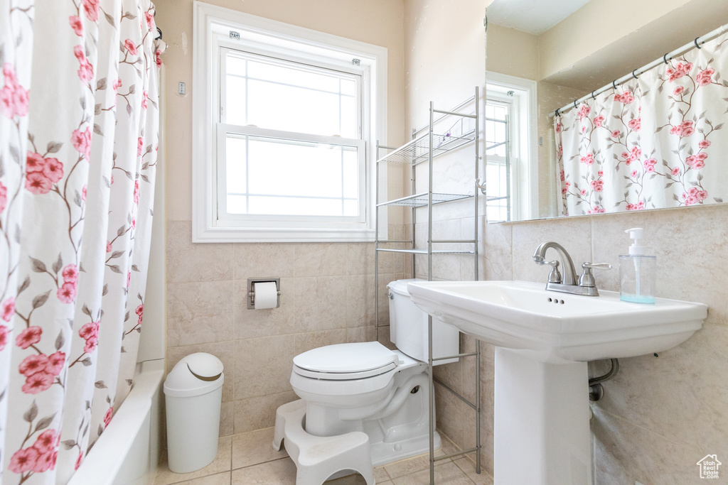 Bathroom featuring shower / bathtub combination with curtain, toilet, tile flooring, and tile walls