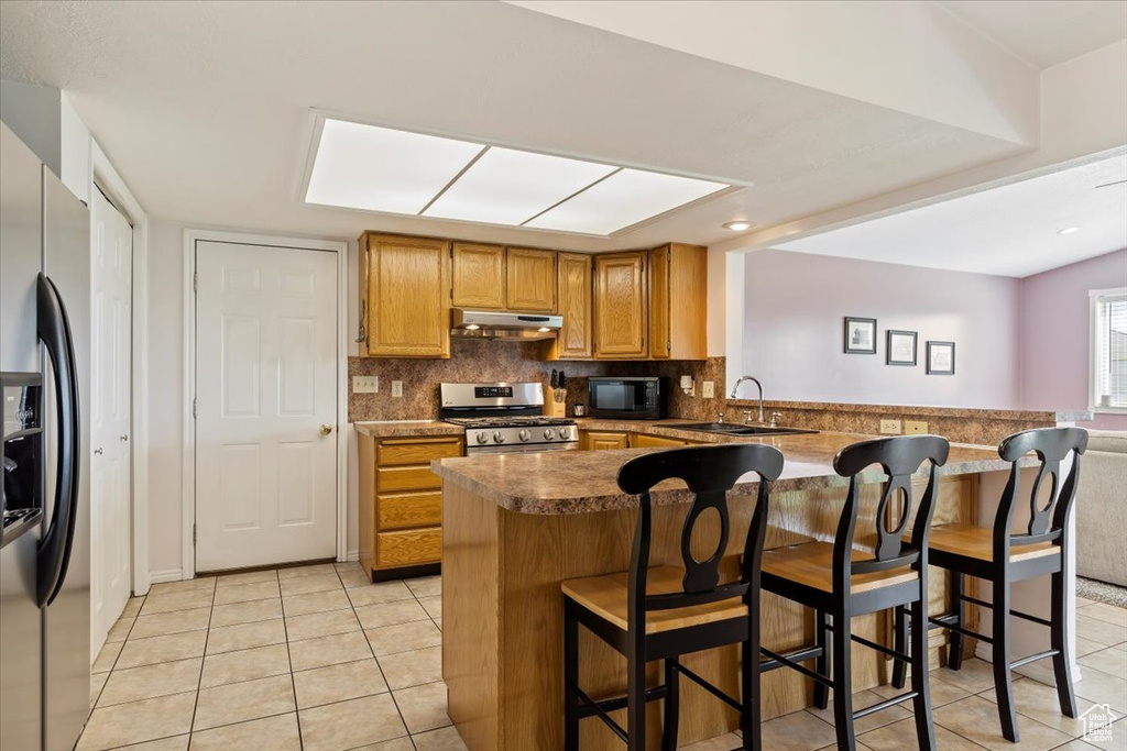 Kitchen featuring kitchen peninsula, stainless steel appliances, tasteful backsplash, sink, and light tile floors
