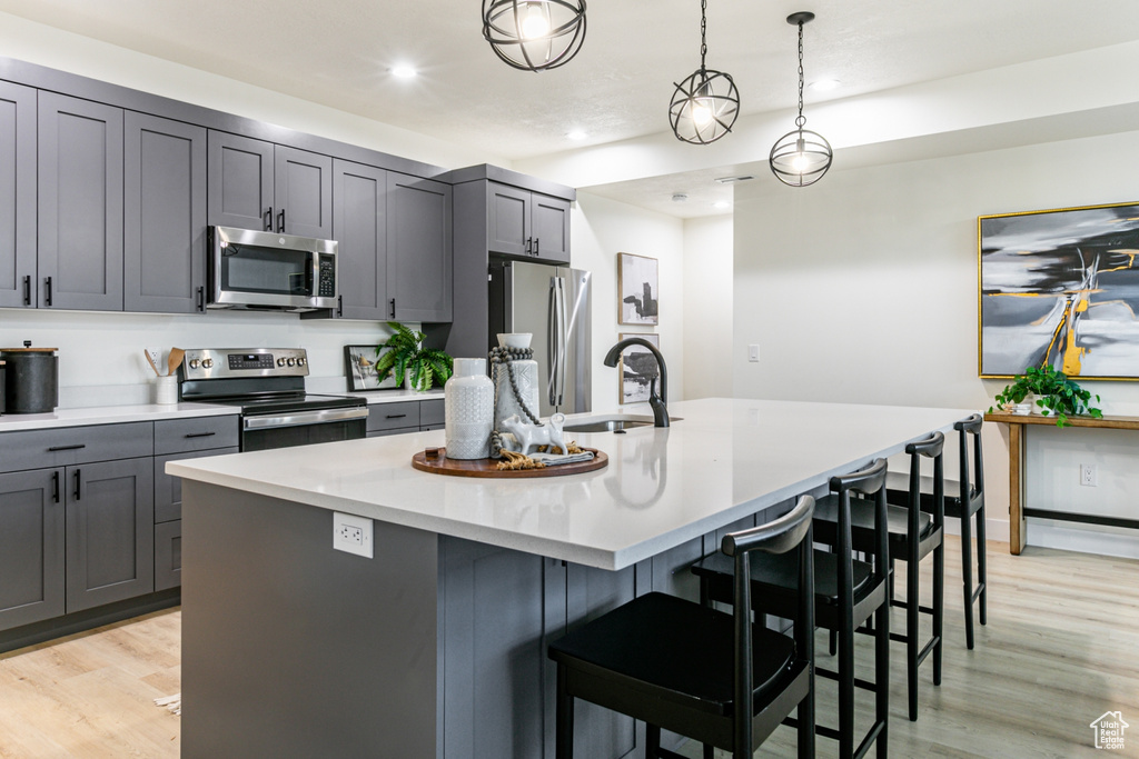 Kitchen featuring appliances with stainless steel finishes, light hardwood / wood-style flooring, hanging light fixtures, a center island with sink, and sink
