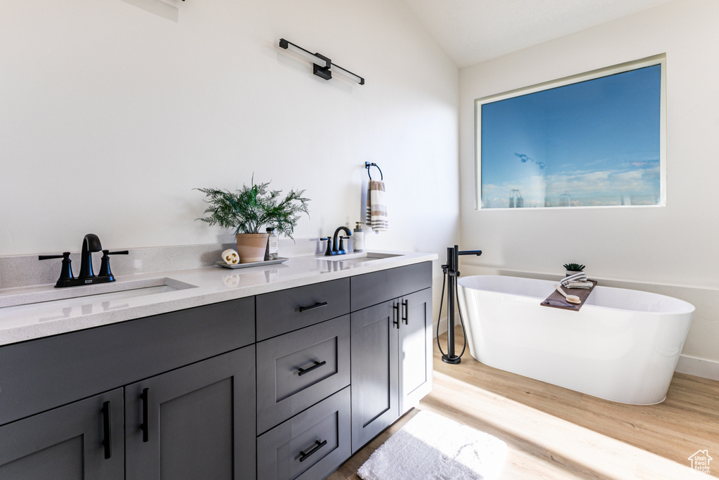 Bathroom with wood-type flooring, dual bowl vanity, and a bathing tub