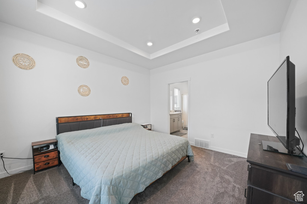 Carpeted bedroom featuring a tray ceiling and connected bathroom