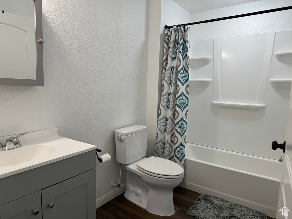 Full bathroom with wood-type flooring, shower / bath combination with curtain, vanity with extensive cabinet space, and toilet