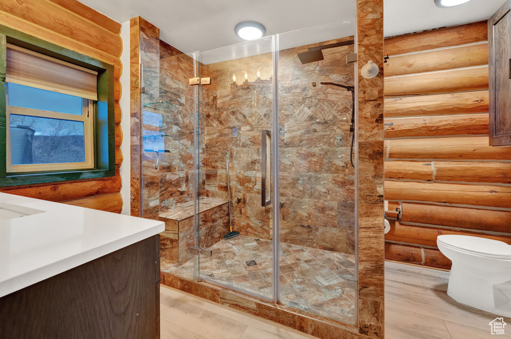 Bathroom featuring log walls, vanity, toilet, and walk in shower