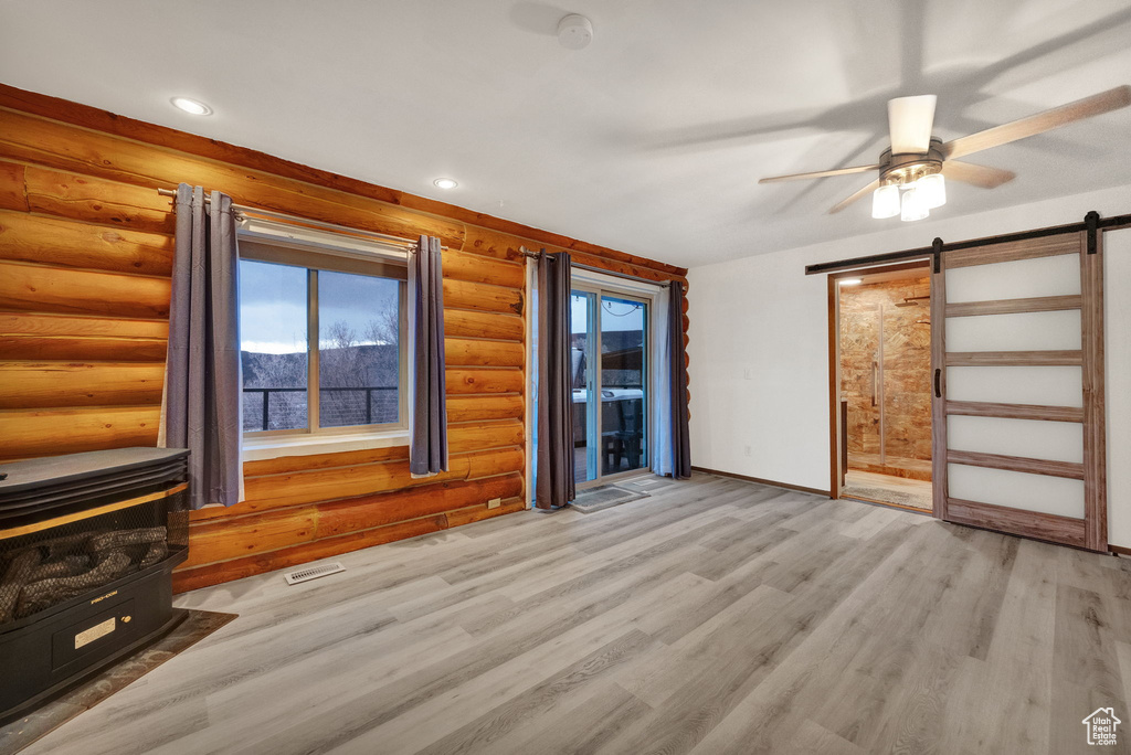 Spare room featuring plenty of natural light, a barn door, log walls, and light wood-type flooring