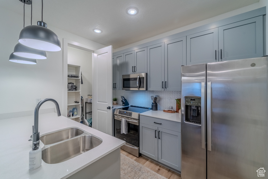 Kitchen with appliances with stainless steel finishes, hanging light fixtures, light hardwood / wood-style floors, tasteful backsplash, and sink