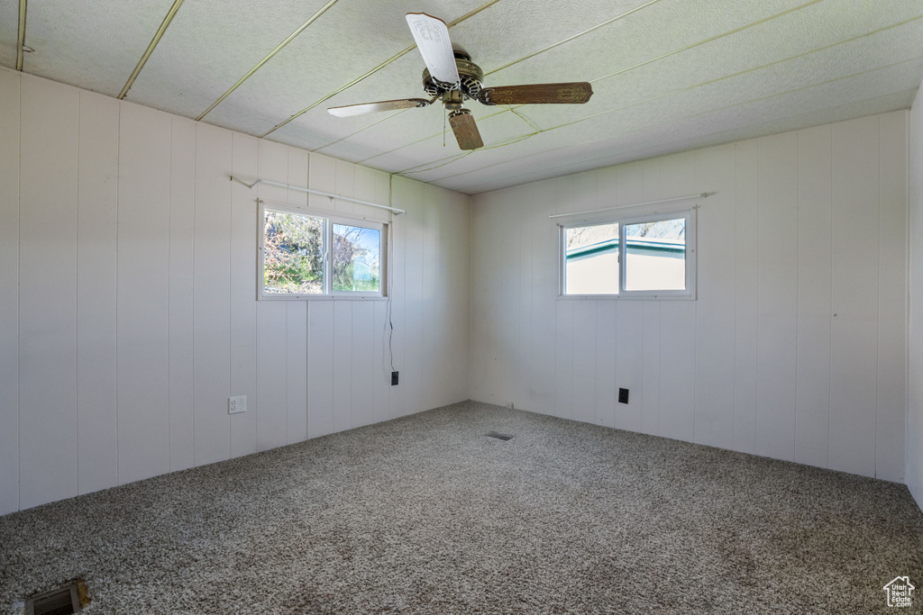 Spare room featuring plenty of natural light, ceiling fan, and carpet floors