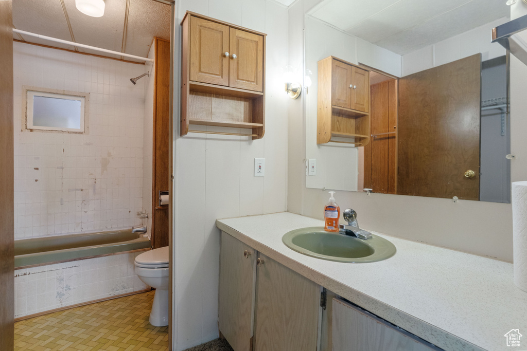 Full bathroom featuring large vanity, tile floors, toilet, and tiled shower / bath