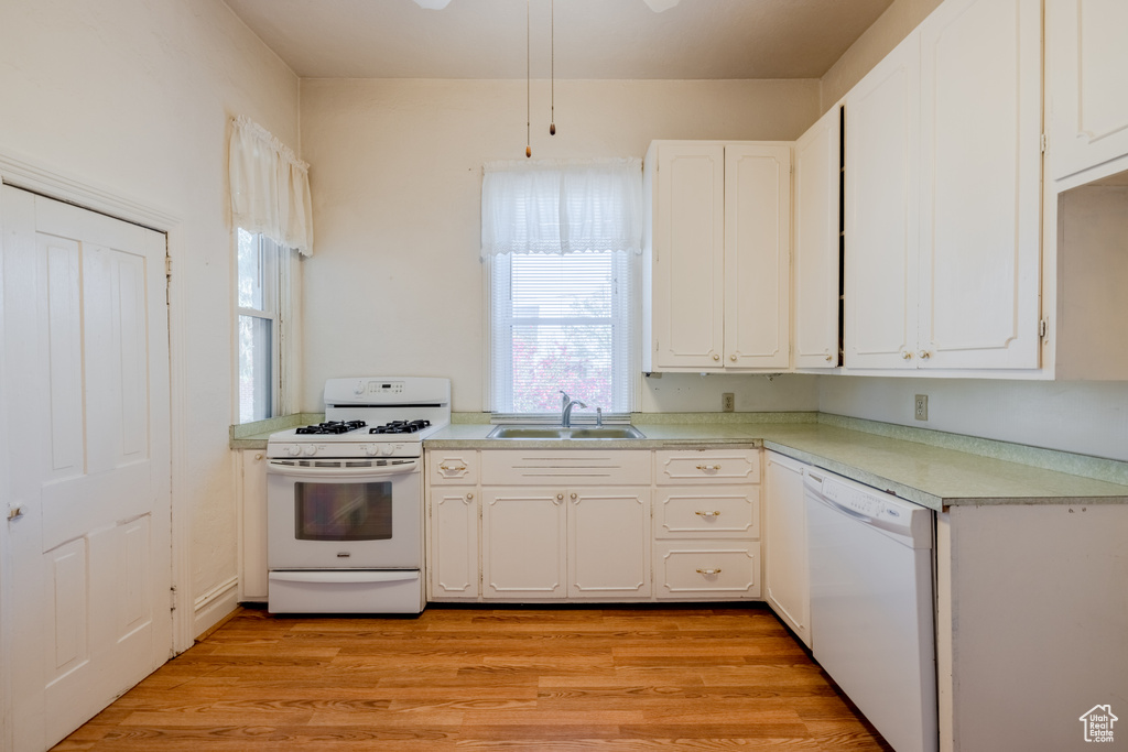 Kitchen with white cabinets, white appliances, sink, and light wood-type flooring