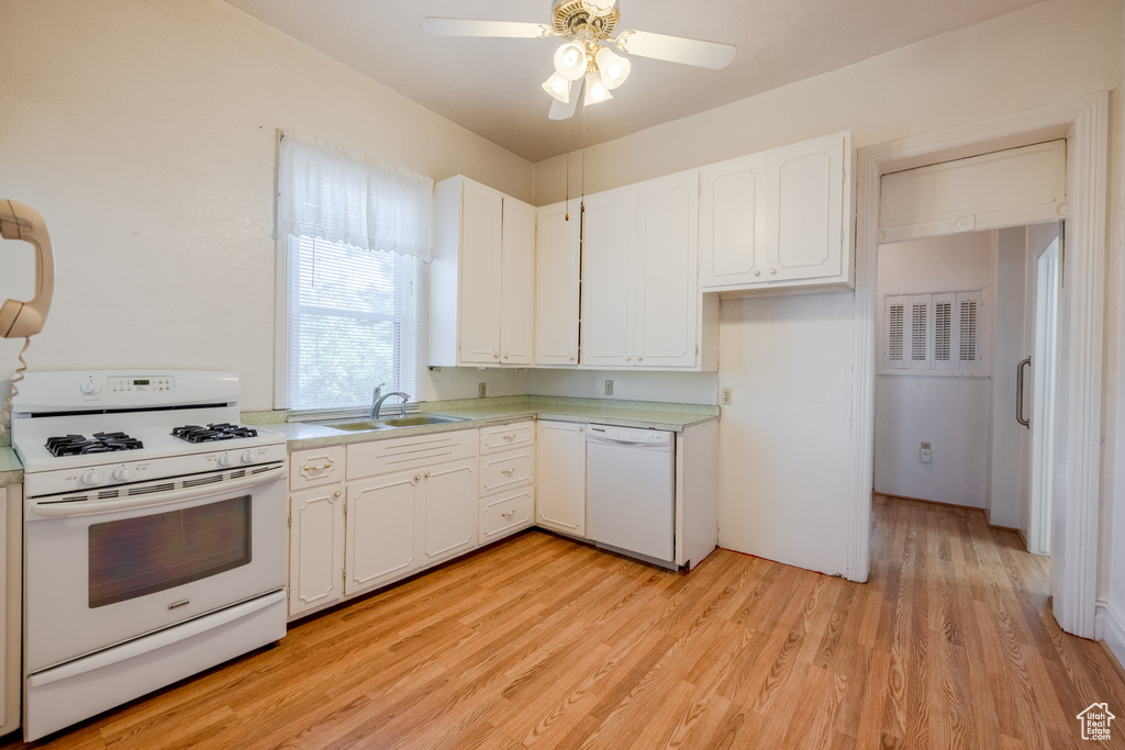 Kitchen featuring white cabinets, sink, white appliances, and light wood-type flooring