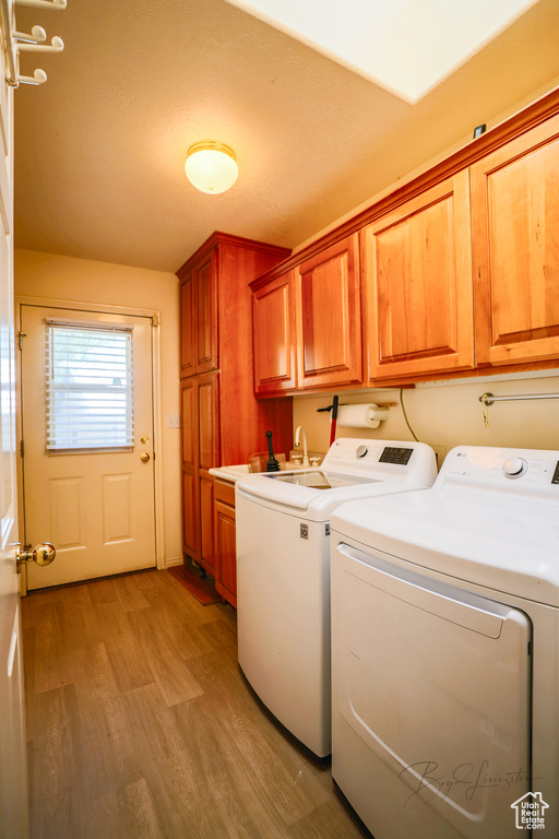Laundry room with cabinets, sink, light hardwood / wood-style floors, and washing machine and dryer