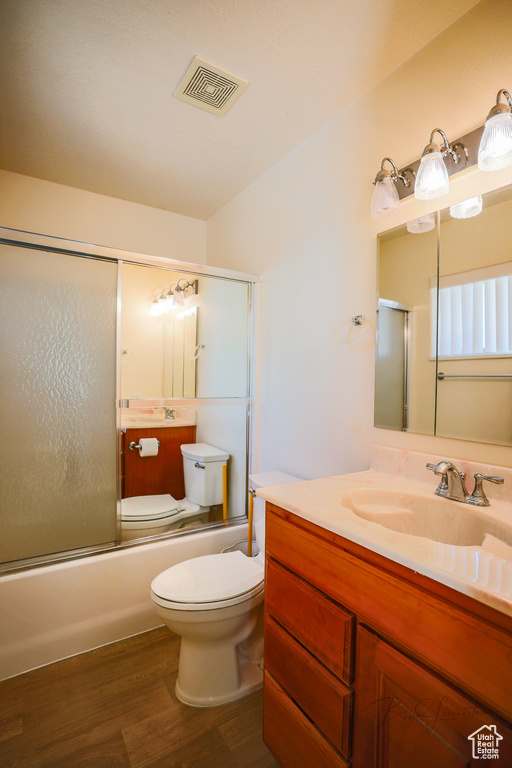 Full bathroom featuring bath / shower combo with glass door, toilet, oversized vanity, and wood-type flooring