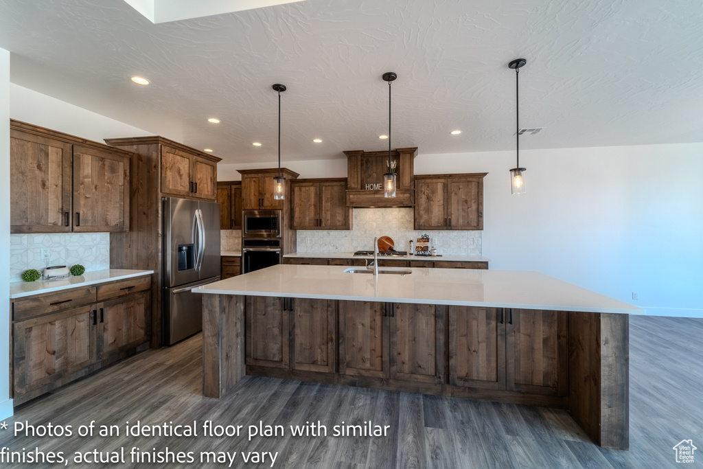 Kitchen featuring appliances with stainless steel finishes, a large island with sink, tasteful backsplash, and dark hardwood / wood-style flooring