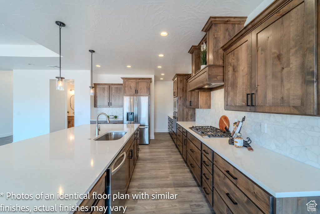 Kitchen with decorative light fixtures, hardwood / wood-style floors, backsplash, stainless steel appliances, and sink