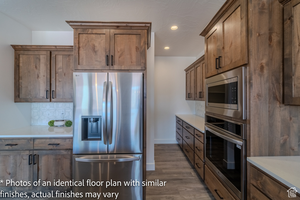 Kitchen with appliances with stainless steel finishes, hardwood / wood-style floors, and backsplash