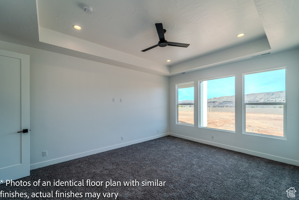 Carpeted spare room featuring ceiling fan, a raised ceiling, and a water view