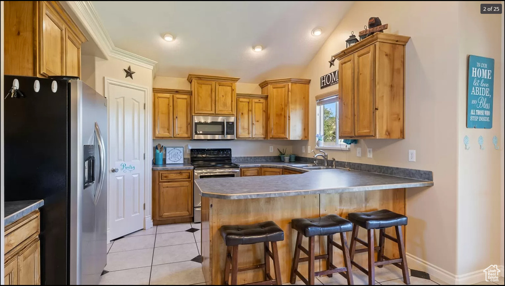 Kitchen with appliances with stainless steel finishes, light tile floors, a kitchen bar, sink, and vaulted ceiling