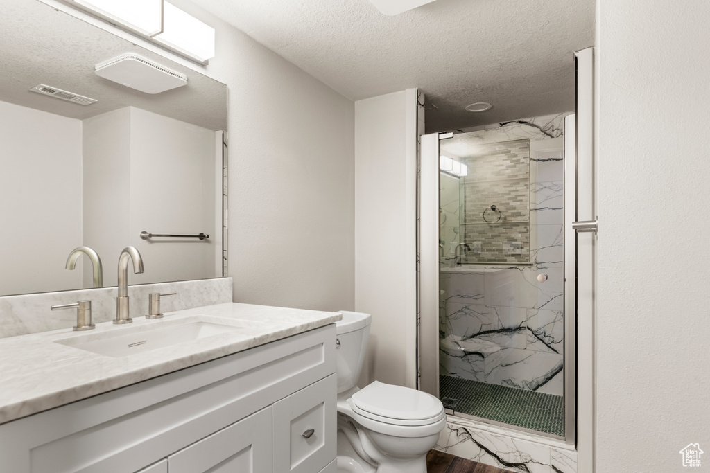 Bathroom featuring a textured ceiling, a shower with shower door, toilet, and vanity with extensive cabinet space