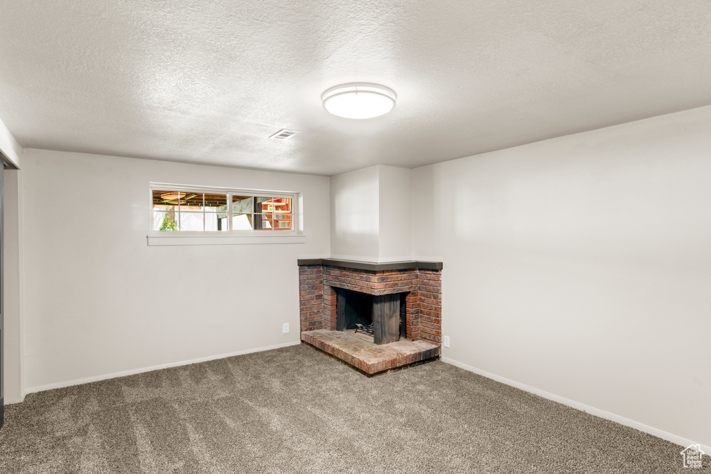 Unfurnished living room with a fireplace, carpet floors, and a textured ceiling