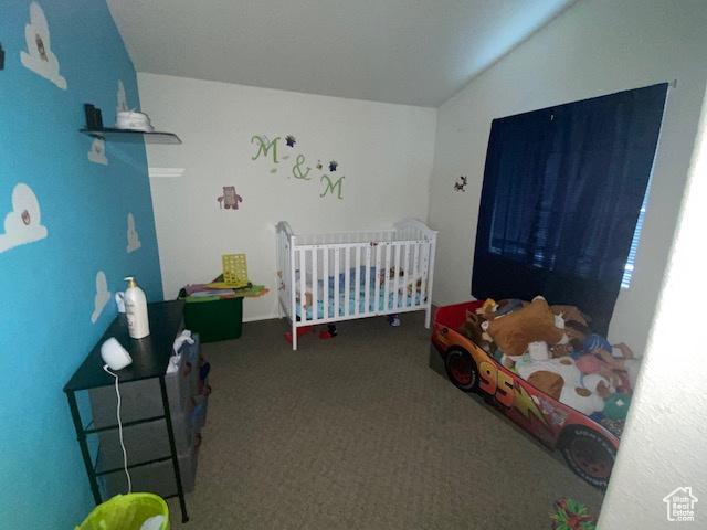 Carpeted bedroom featuring lofted ceiling and a nursery area