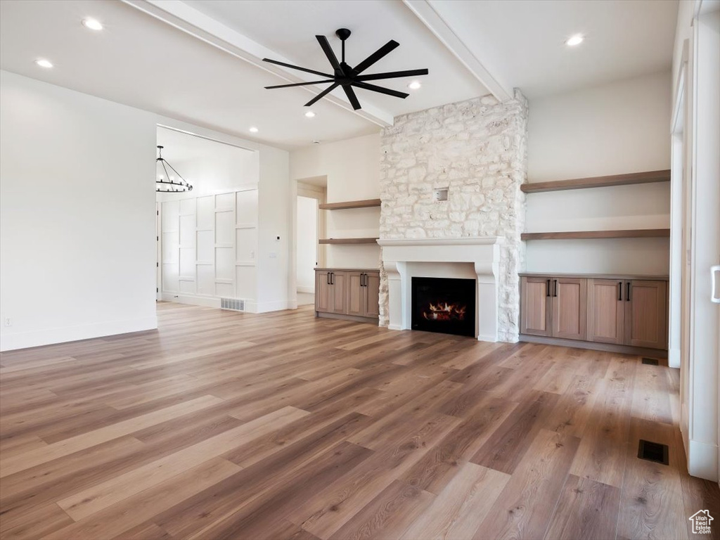 Unfurnished living room featuring beamed ceiling, ceiling fan, hardwood / wood-style flooring, and a stone fireplace