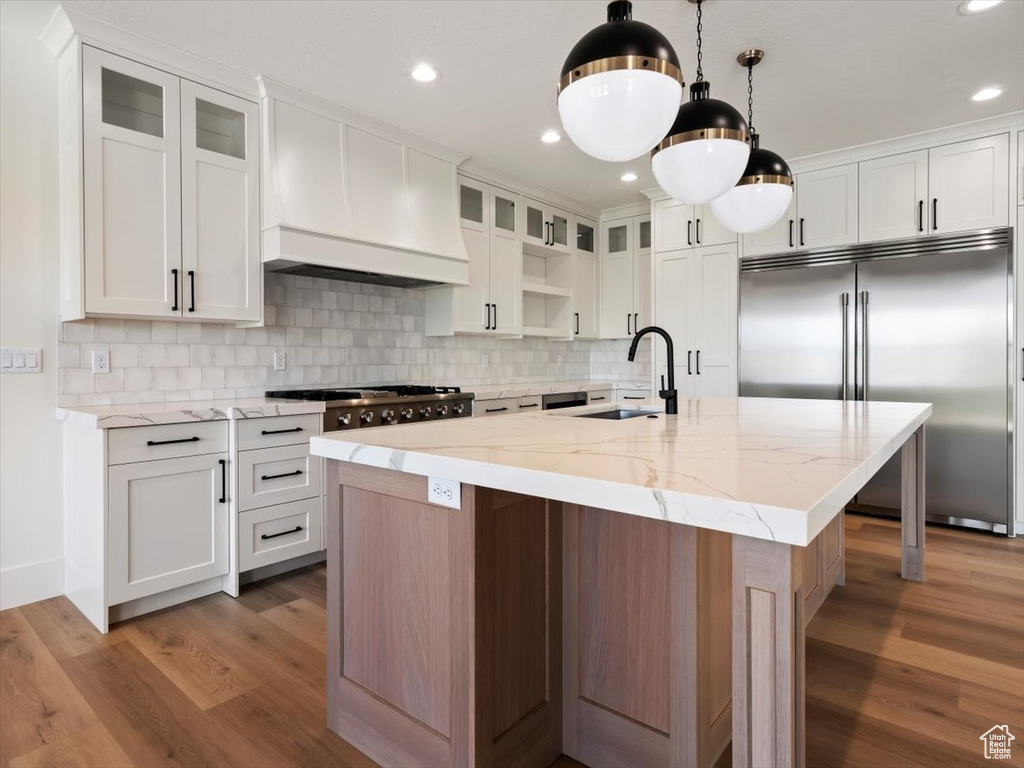 Kitchen featuring tasteful backsplash, built in refrigerator, wood-type flooring, and custom exhaust hood