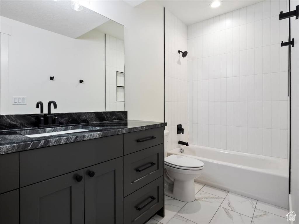 Full bathroom with tiled shower / bath combo, vanity, tile floors, and toilet