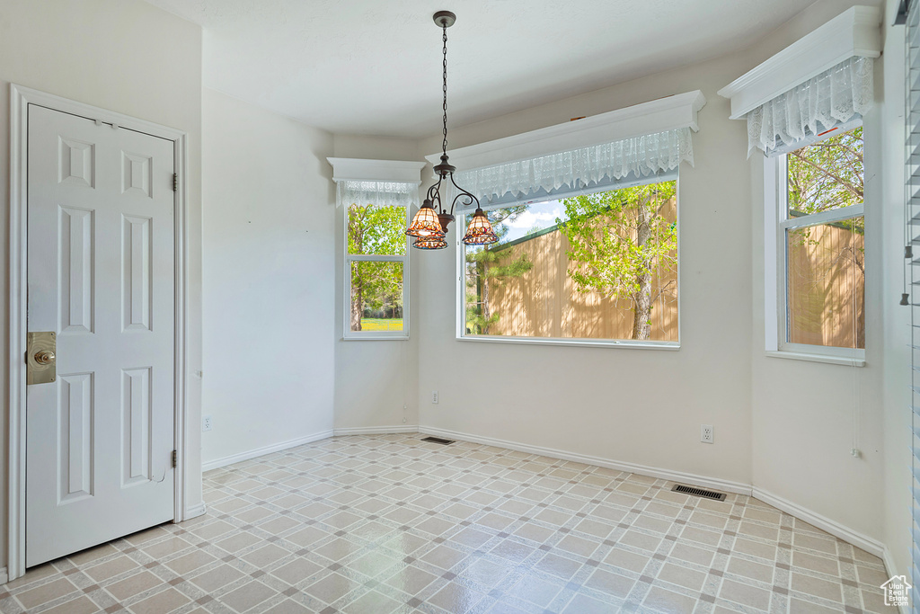 Unfurnished dining area with a healthy amount of sunlight, a notable chandelier, and light tile flooring