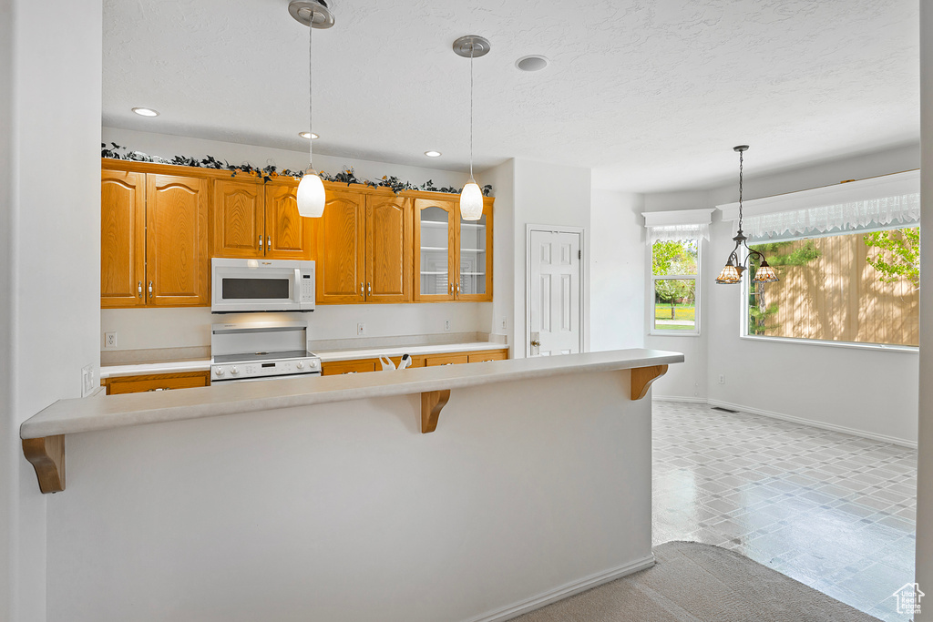 Kitchen featuring decorative light fixtures, white appliances, light tile floors, and a breakfast bar