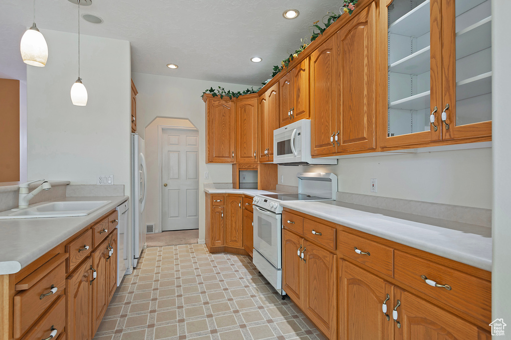 Kitchen with sink, white appliances, light tile floors, and pendant lighting