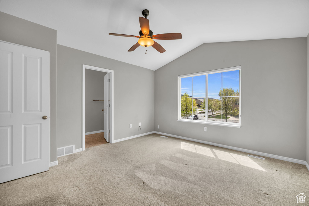 Unfurnished bedroom featuring carpet, ceiling fan, a walk in closet, and lofted ceiling