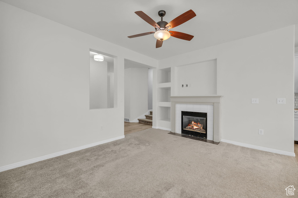 Unfurnished living room featuring light colored carpet, a fireplace, ceiling fan, and built in features
