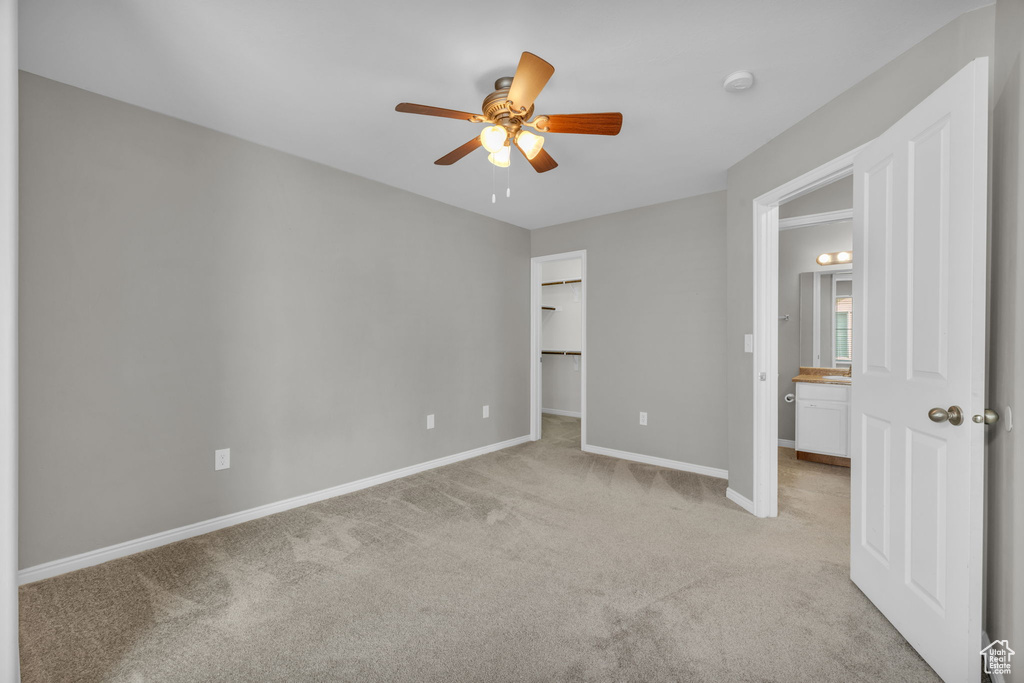 Unfurnished bedroom with light colored carpet, a walk in closet, ceiling fan, and a closet