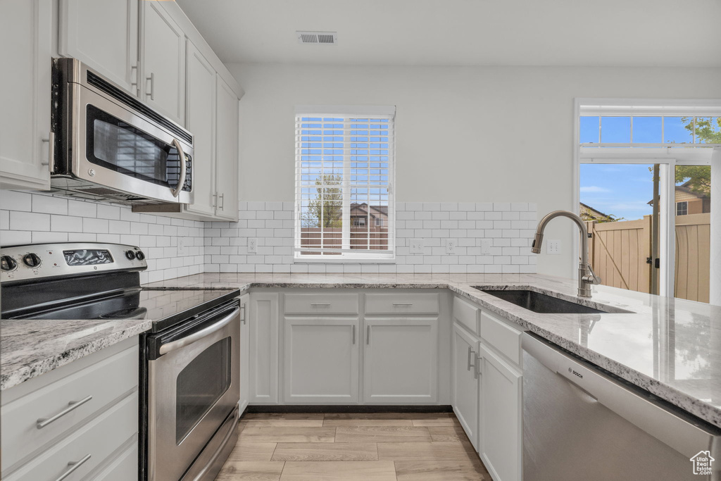 Kitchen featuring tasteful backsplash, stainless steel appliances, white cabinets, and sink