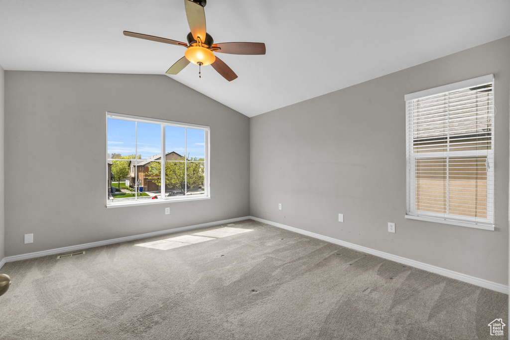 Empty room with vaulted ceiling, ceiling fan, and carpet flooring