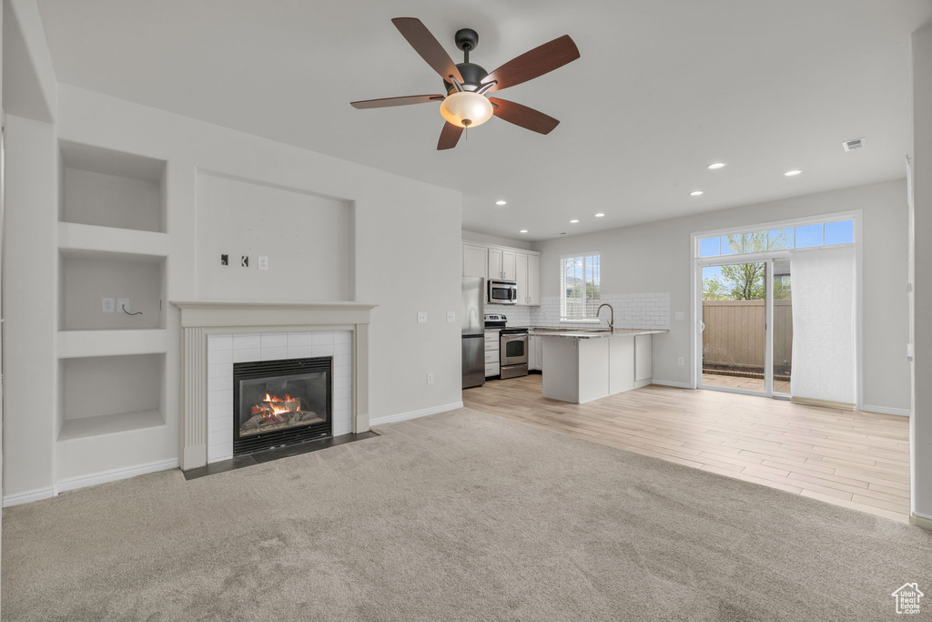 Unfurnished living room featuring light colored carpet, a fireplace, and ceiling fan