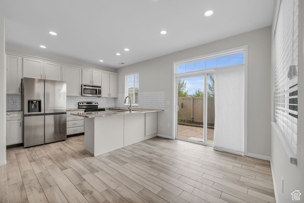 Kitchen featuring kitchen peninsula, light hardwood / wood-style flooring, stainless steel appliances, tasteful backsplash, and white cabinetry