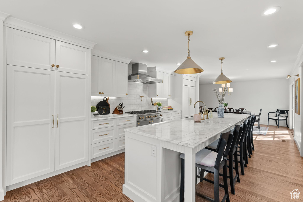 Kitchen with white cabinets, sink, light wood-type flooring, and wall chimney exhaust hood