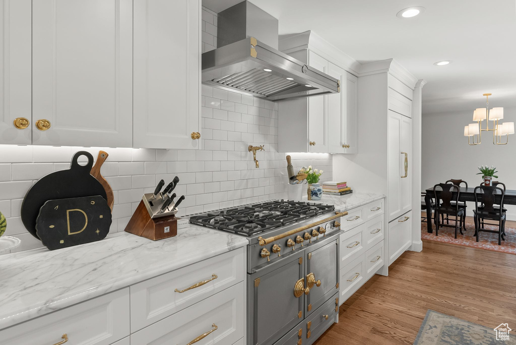 Kitchen featuring light wood-type flooring, backsplash, wall chimney exhaust hood, and white cabinetry