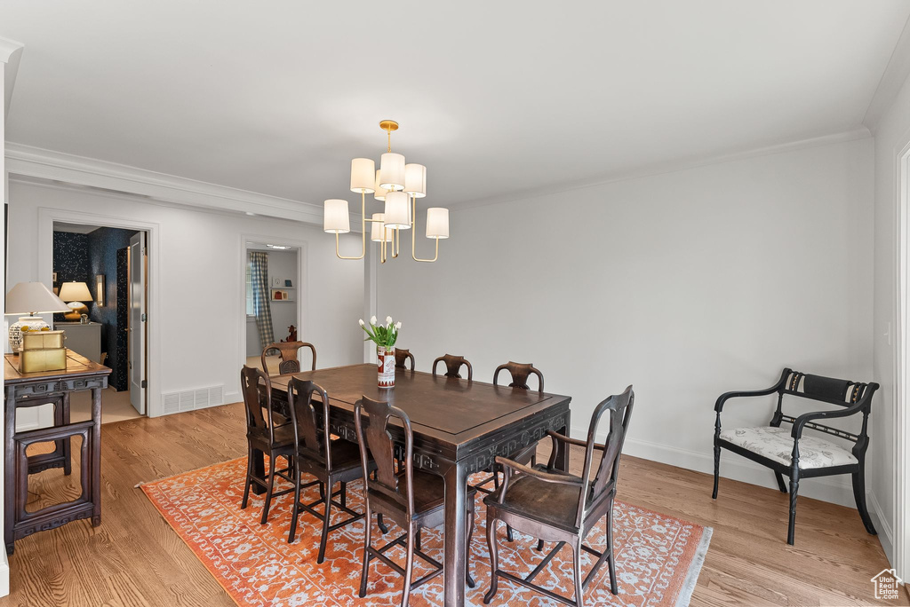 Dining space with an inviting chandelier, light hardwood / wood-style flooring, and crown molding