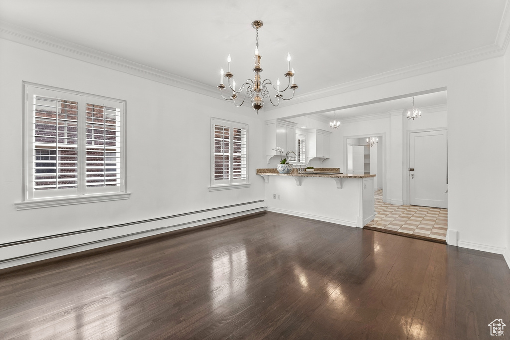 Unfurnished living room with dark hardwood / wood-style floors, crown molding, an inviting chandelier, and plenty of natural light