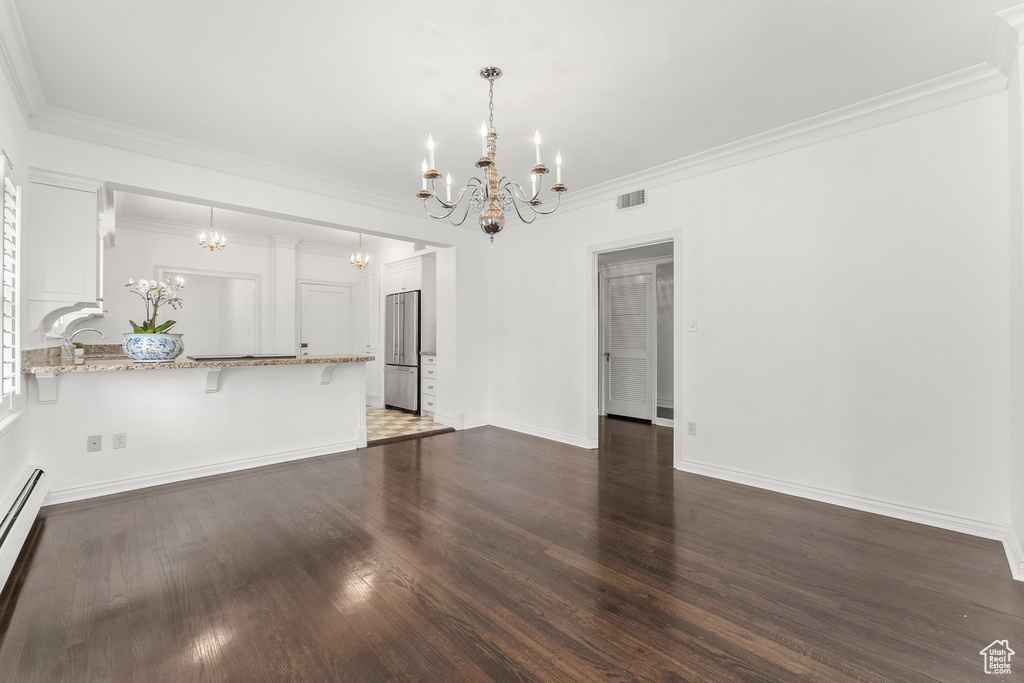 Unfurnished living room featuring dark wood-type flooring, a baseboard heating unit, a chandelier, and ornamental molding