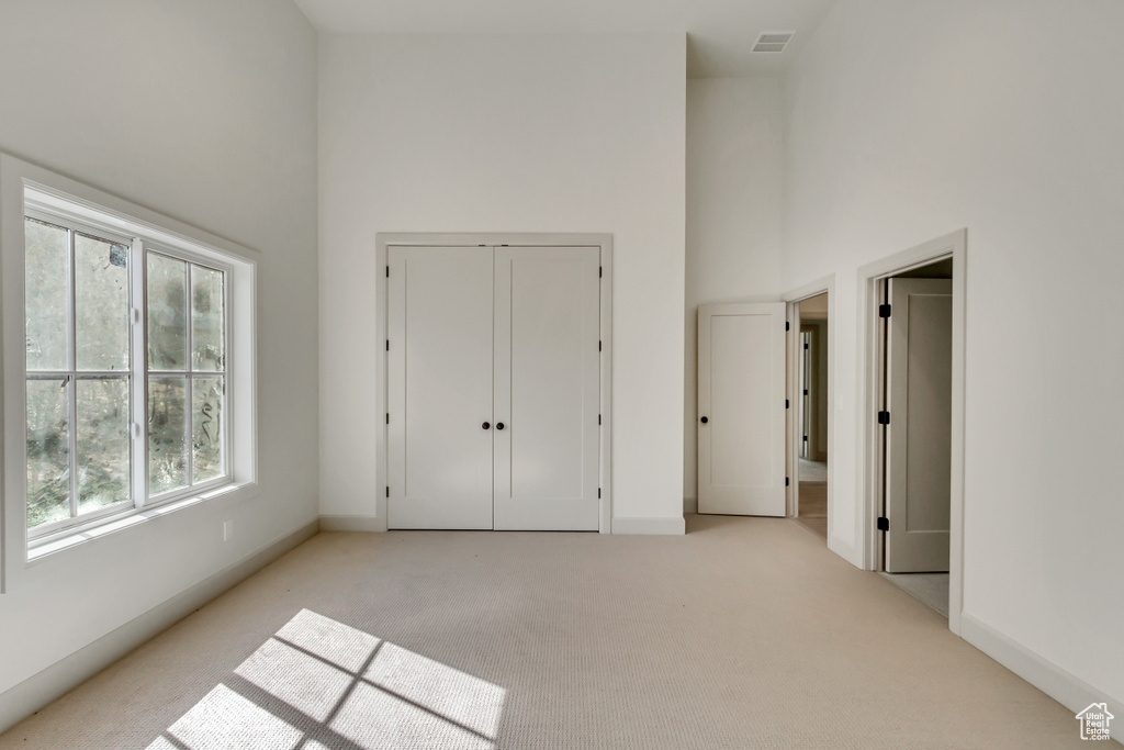 Unfurnished bedroom featuring a towering ceiling, light carpet, and a closet