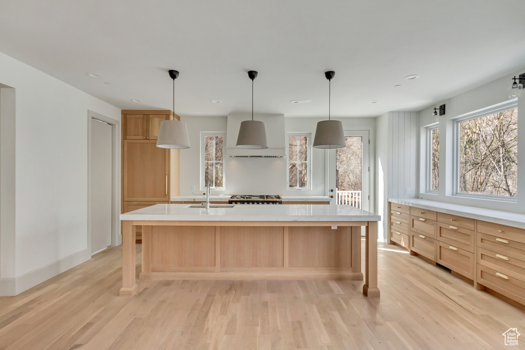 Kitchen with light hardwood / wood-style floors, a center island with sink, and wall chimney range hood