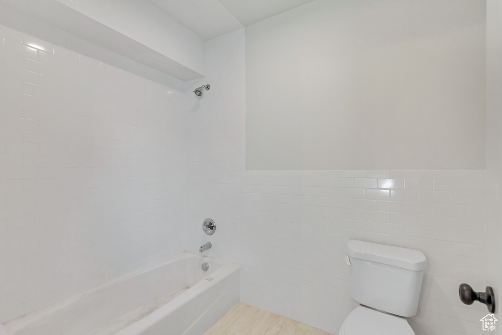 Bathroom featuring toilet, bathtub / shower combination, and tile walls
