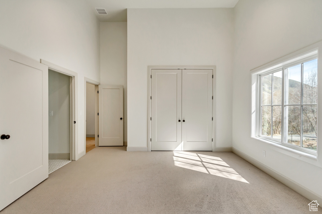 Unfurnished bedroom featuring light colored carpet, a towering ceiling, and a closet