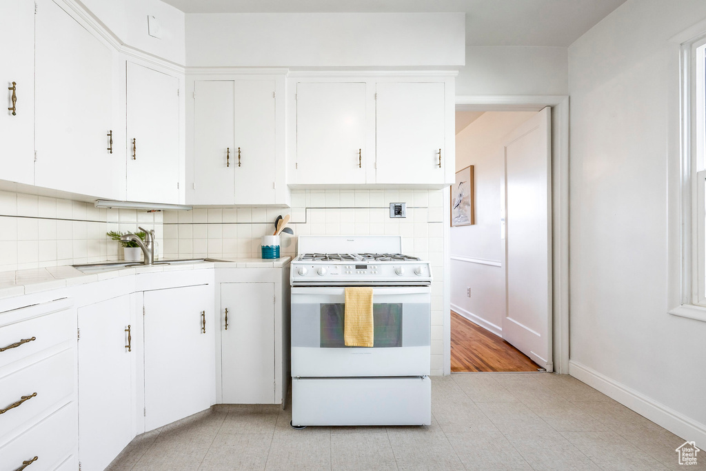 Kitchen with white gas range oven, white cabinetry, light tile floors, tasteful backsplash, and tile countertops