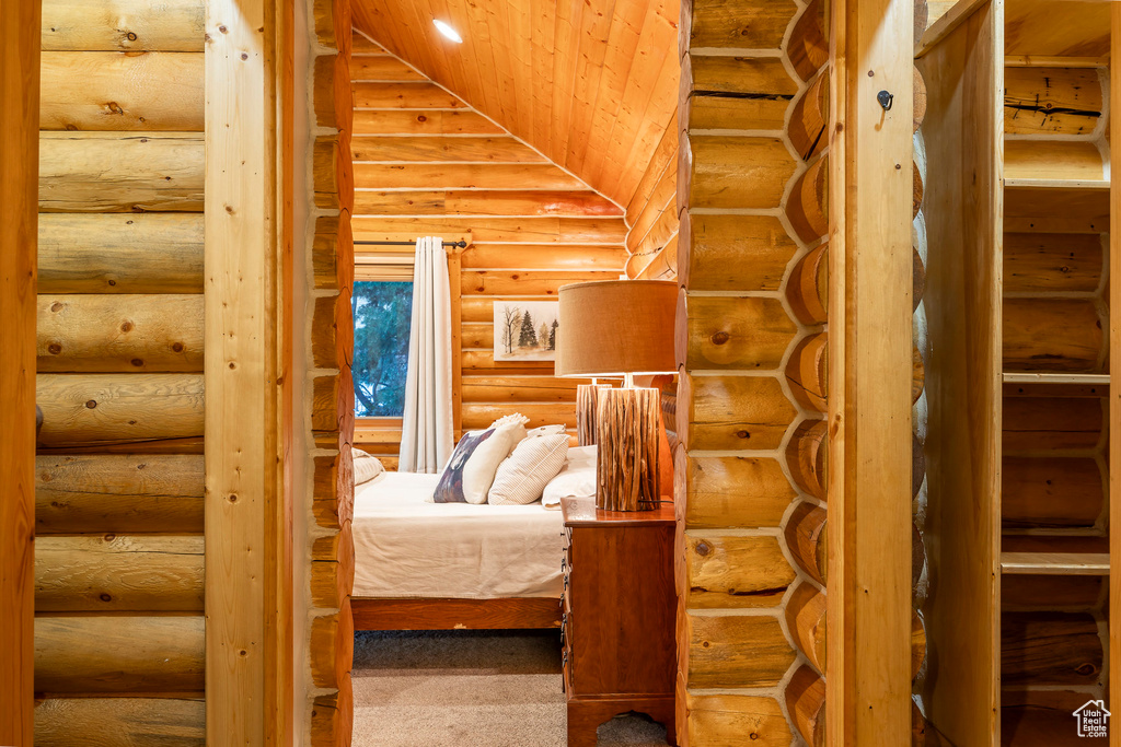 Unfurnished bedroom with log walls, carpet, lofted ceiling, and wooden ceiling