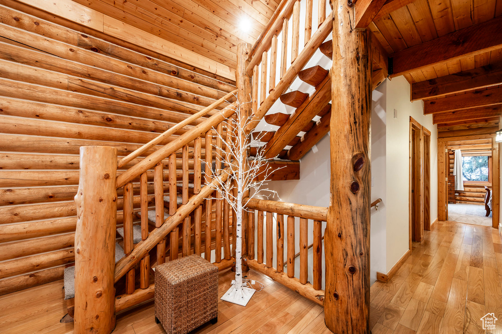 Staircase featuring log walls, beamed ceiling, wooden ceiling, and light wood-type flooring